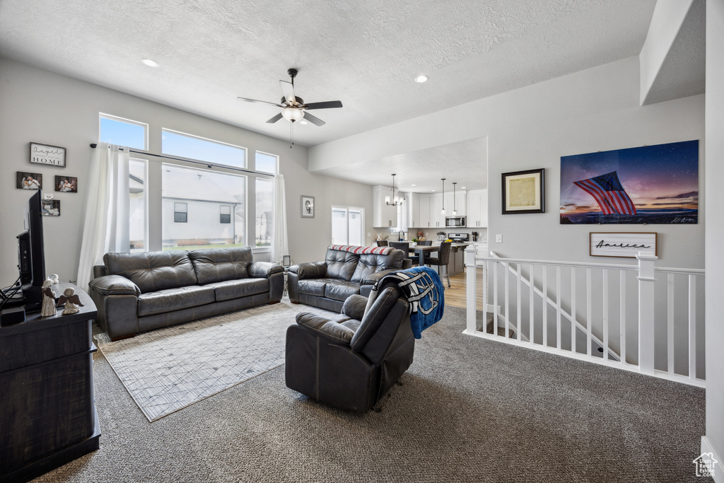 Living room with light colored carpet, a textured ceiling, and ceiling fan with notable chandelier