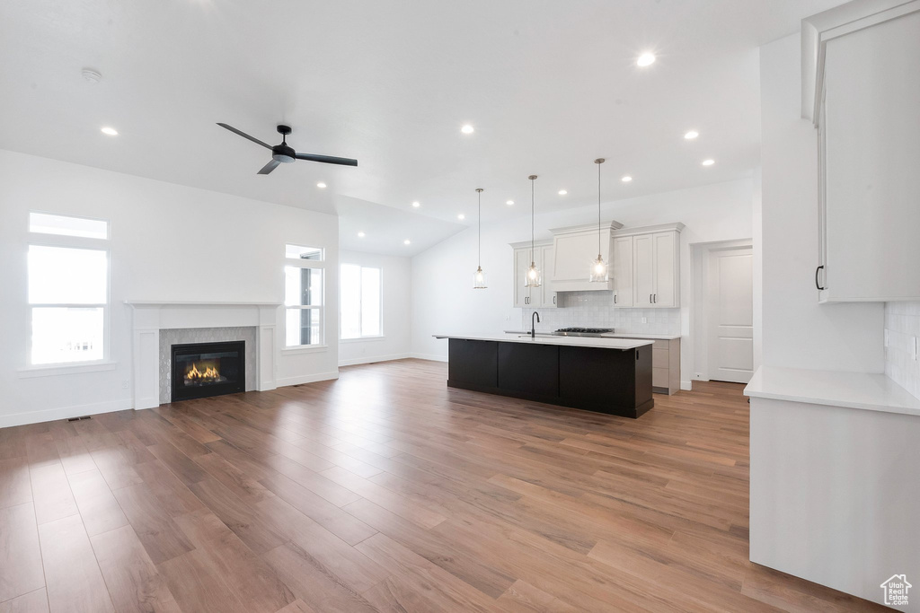 Kitchen featuring hanging light fixtures, light hardwood / wood-style flooring, white cabinetry, ceiling fan, and a center island with sink