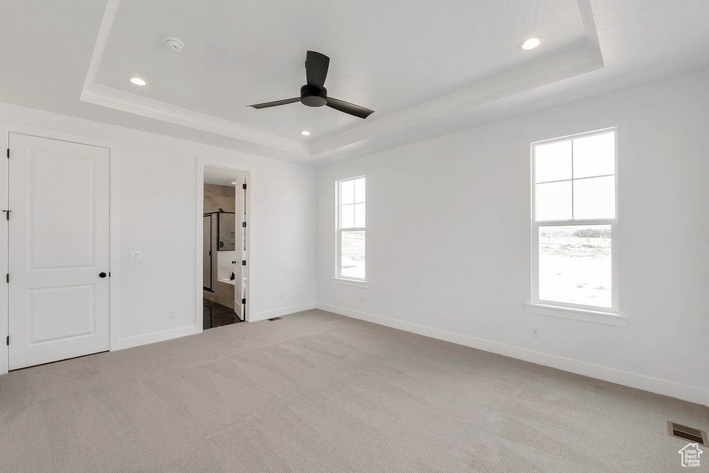 Unfurnished bedroom featuring ensuite bath, multiple windows, and a tray ceiling