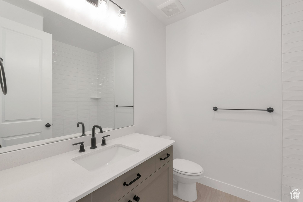 Bathroom with vanity, toilet, wood-type flooring, and a tile shower