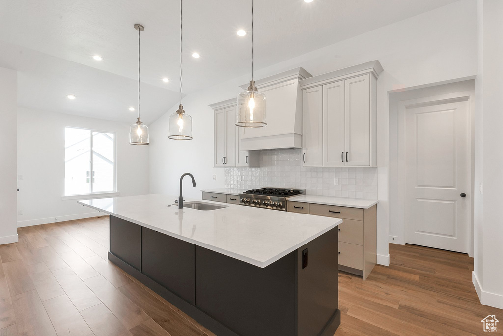 Kitchen featuring an island with sink, hanging light fixtures, custom range hood, and sink