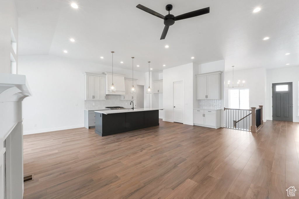 Kitchen with a kitchen island with sink, ceiling fan with notable chandelier, decorative light fixtures, vaulted ceiling, and light hardwood / wood-style floors