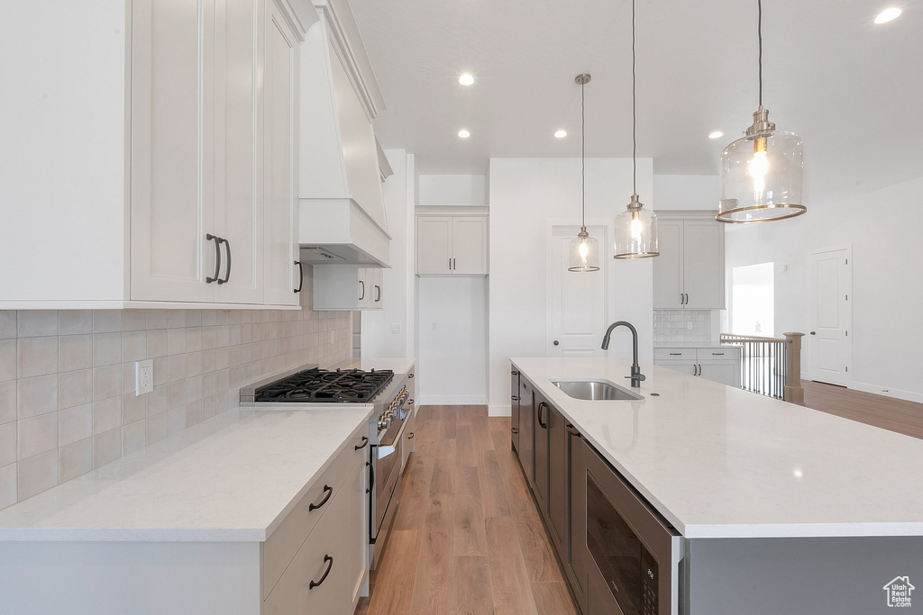 Kitchen with custom exhaust hood, decorative light fixtures, stainless steel appliances, sink, and a center island with sink