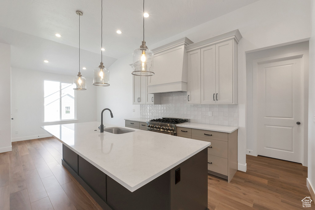 Kitchen with hardwood / wood-style flooring, decorative light fixtures, high end stainless steel range oven, custom exhaust hood, and a center island with sink