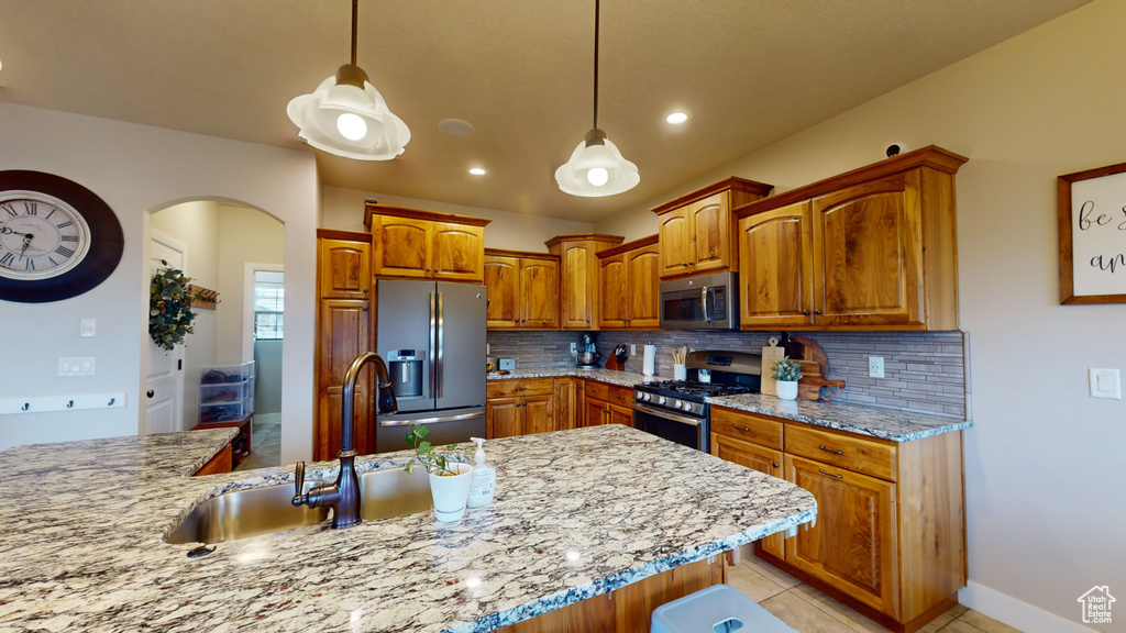 Kitchen featuring decorative backsplash, hanging light fixtures, light tile patterned floors, sink, and stainless steel appliances