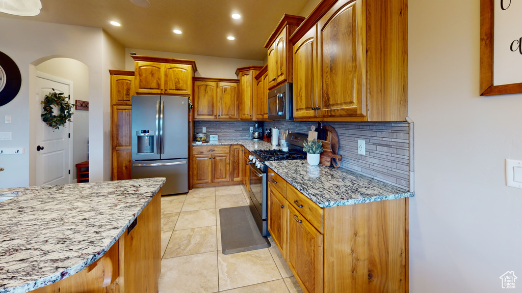 Kitchen with light tile patterned floors, appliances with stainless steel finishes, decorative backsplash, and light stone countertops