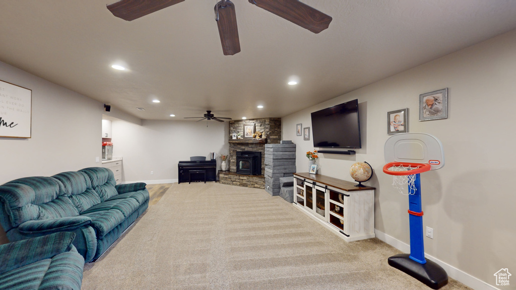 Living room with ceiling fan, a stone fireplace, and light colored carpet