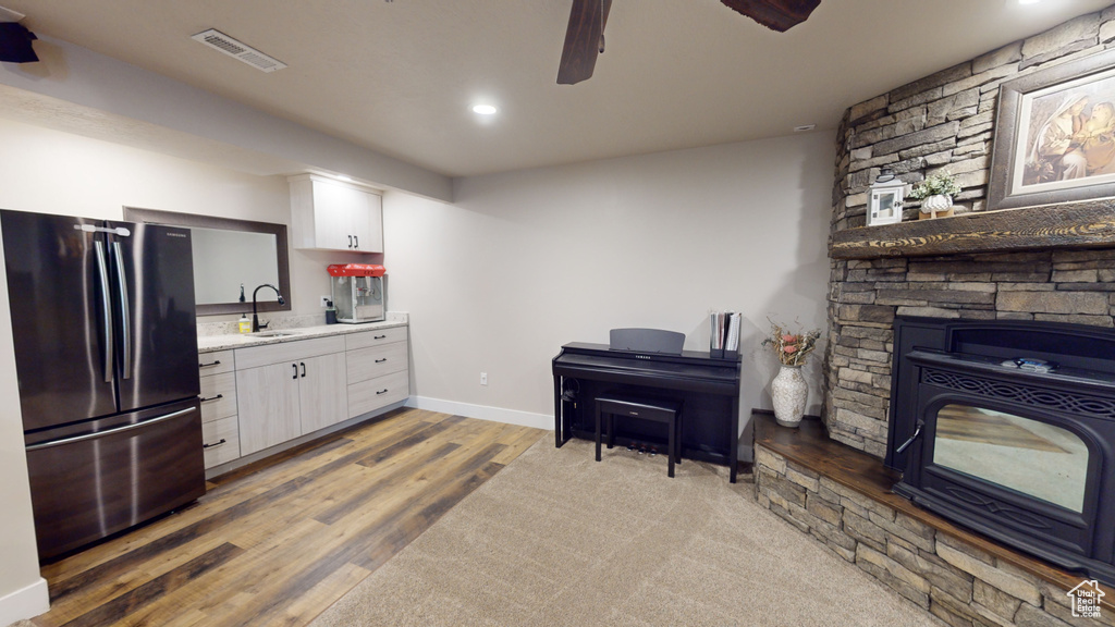 Kitchen featuring ceiling fan, a stone fireplace, black fridge, hardwood / wood-style floors, and sink