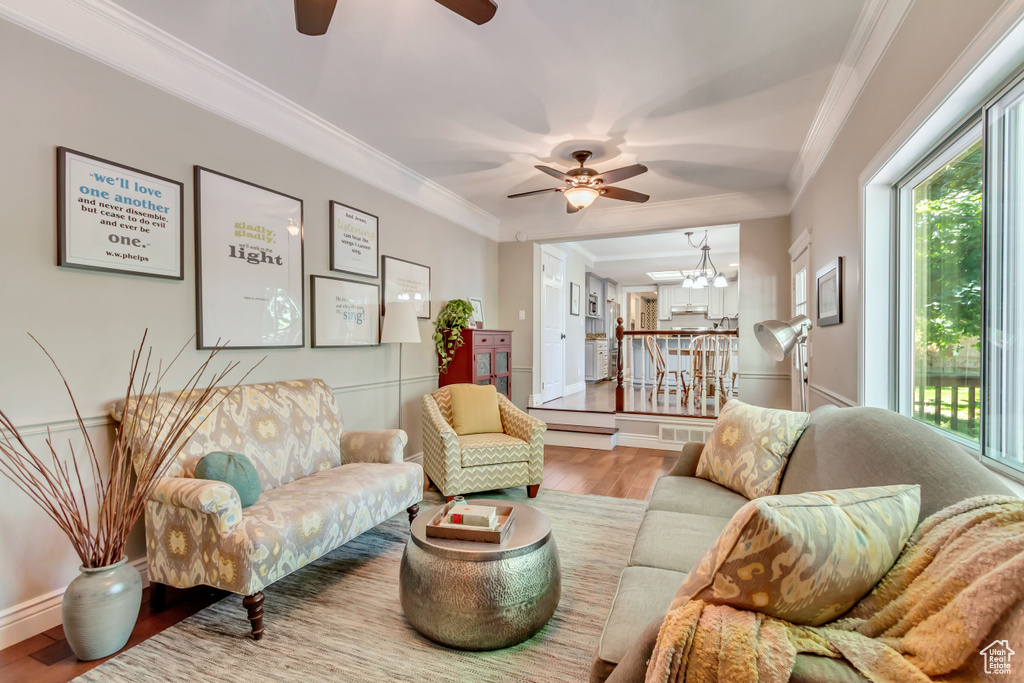 Living room with ceiling fan with notable chandelier, crown molding, and light wood-type flooring