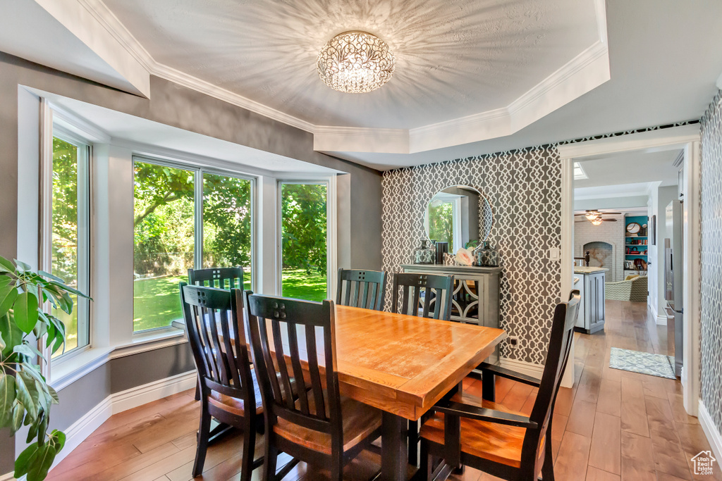 Dining space featuring light wood-type flooring, an inviting chandelier, ornamental molding, and a tray ceiling