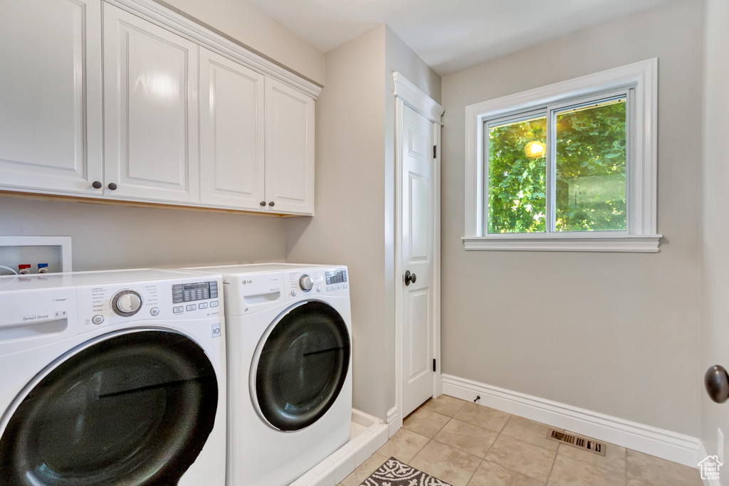 Clothes washing area with light tile patterned floors, cabinets, and washer and dryer