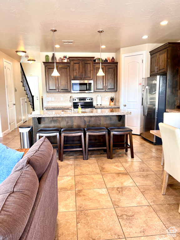 Kitchen featuring appliances with stainless steel finishes, decorative backsplash, light tile patterned flooring, and light stone countertops