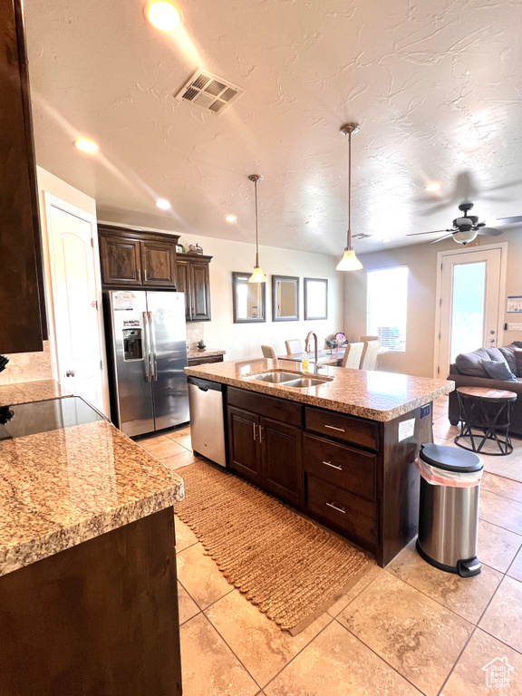 Kitchen featuring ceiling fan, appliances with stainless steel finishes, light tile patterned floors, sink, and a center island with sink