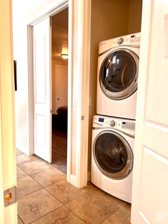 Clothes washing area with stacked washer and clothes dryer and light tile patterned floors