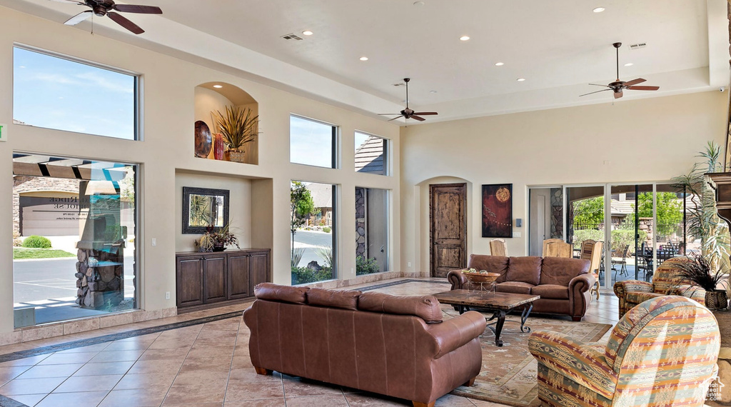 Tiled living room featuring ceiling fan, a raised ceiling, and a towering ceiling