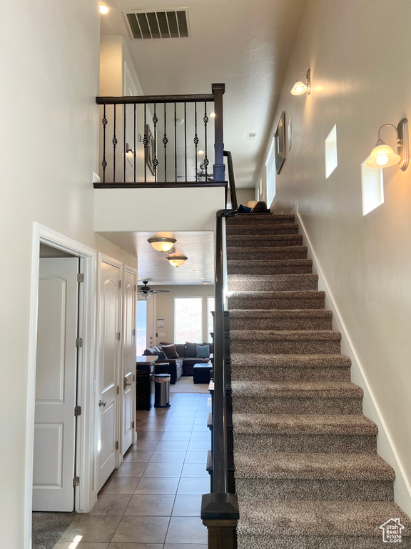 Staircase with tile patterned flooring, ceiling fan, and a towering ceiling