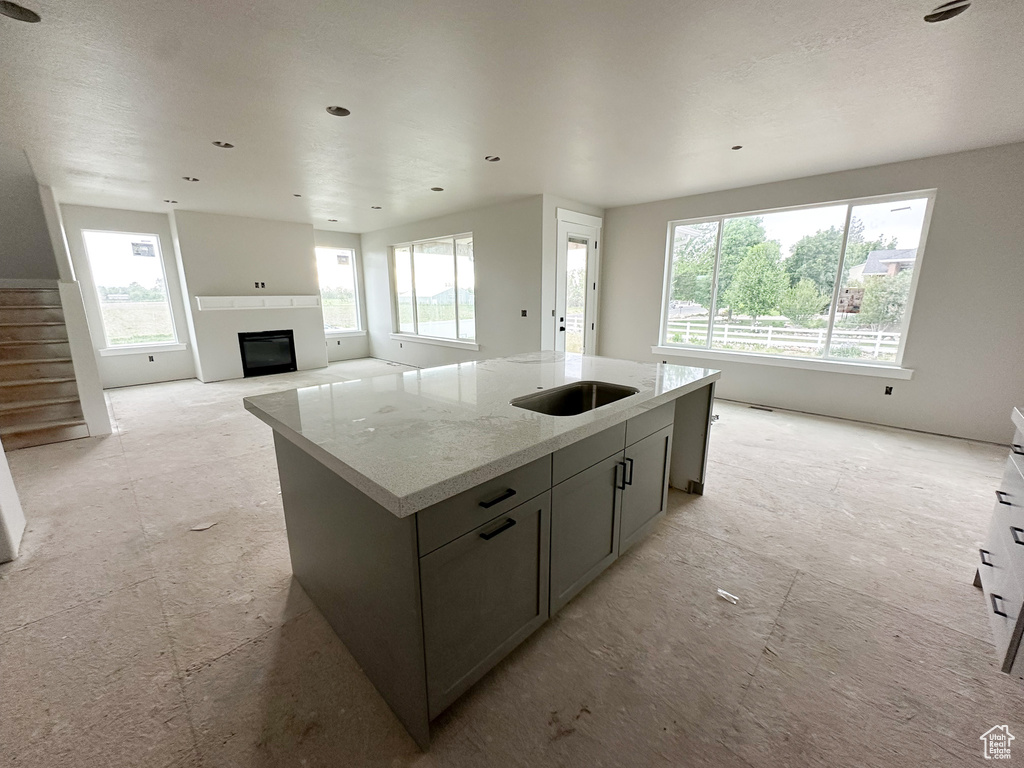 Kitchen with a sink, a glass covered fireplace, a kitchen island with sink, light stone countertops, and open floor plan