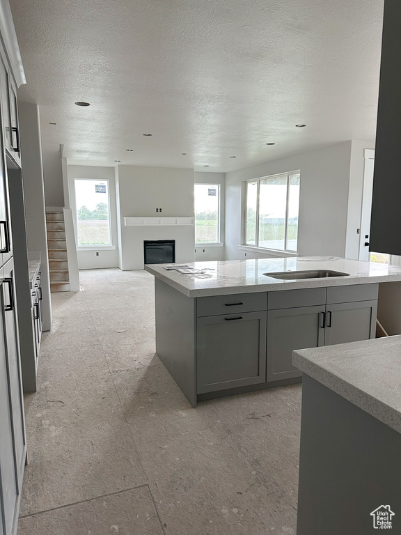 Kitchen featuring a glass covered fireplace, healthy amount of natural light, a textured ceiling, a center island, and light stone counters