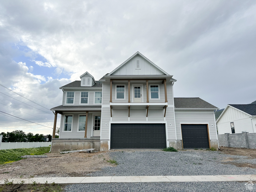 View of front facade with covered porch, fence, gravel driveway, and an attached garage