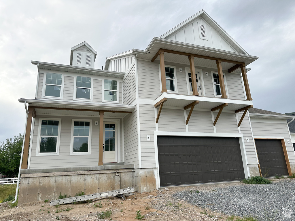 View of front facade with a porch, driveway, board and batten siding, and a garage