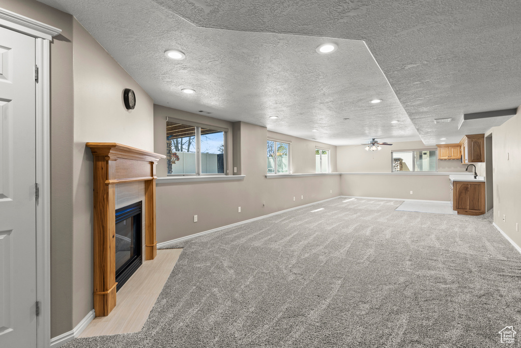 Unfurnished living room featuring baseboards, a textured ceiling, a fireplace with flush hearth, and ceiling fan