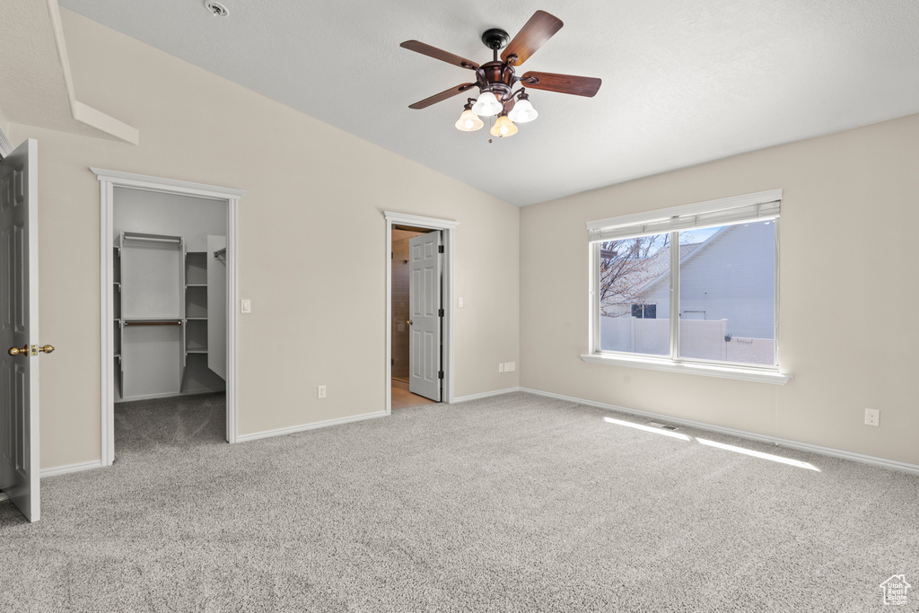 Unfurnished bedroom with carpet floors, baseboards, a walk in closet, a ceiling fan, and vaulted ceiling