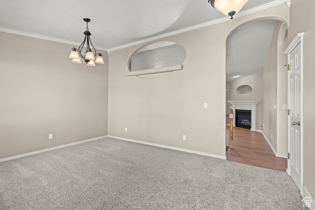 Spare room featuring carpet floors, baseboards, a notable chandelier, a glass covered fireplace, and ornamental molding
