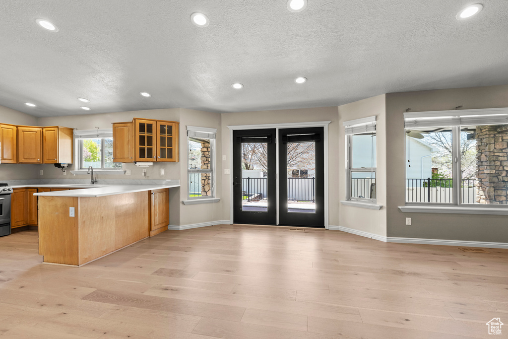 Kitchen featuring a sink, light countertops, light wood finished floors, a peninsula, and glass insert cabinets