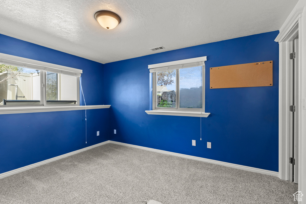 Carpeted spare room featuring baseboards, a textured ceiling, and visible vents