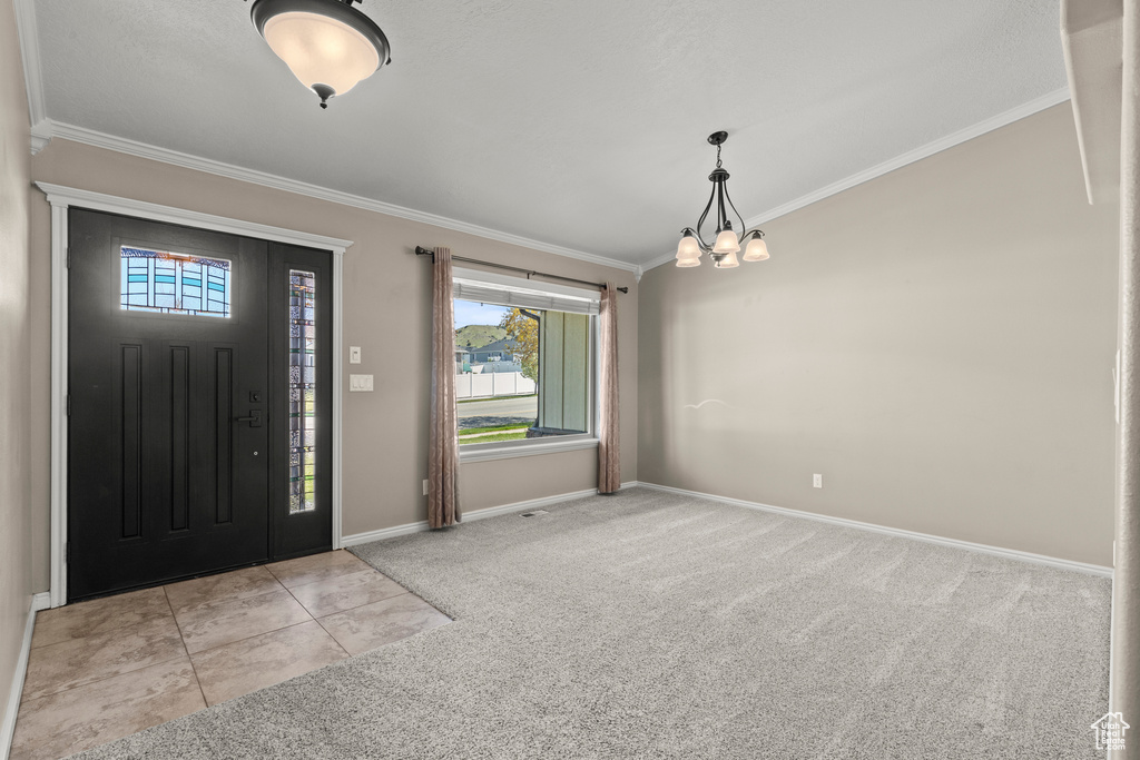 Carpeted entrance foyer with crown molding, baseboards, and a chandelier