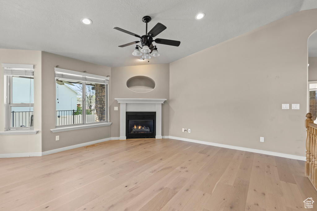 Unfurnished living room featuring a glass covered fireplace, baseboards, ceiling fan, a textured ceiling, and light wood-style flooring