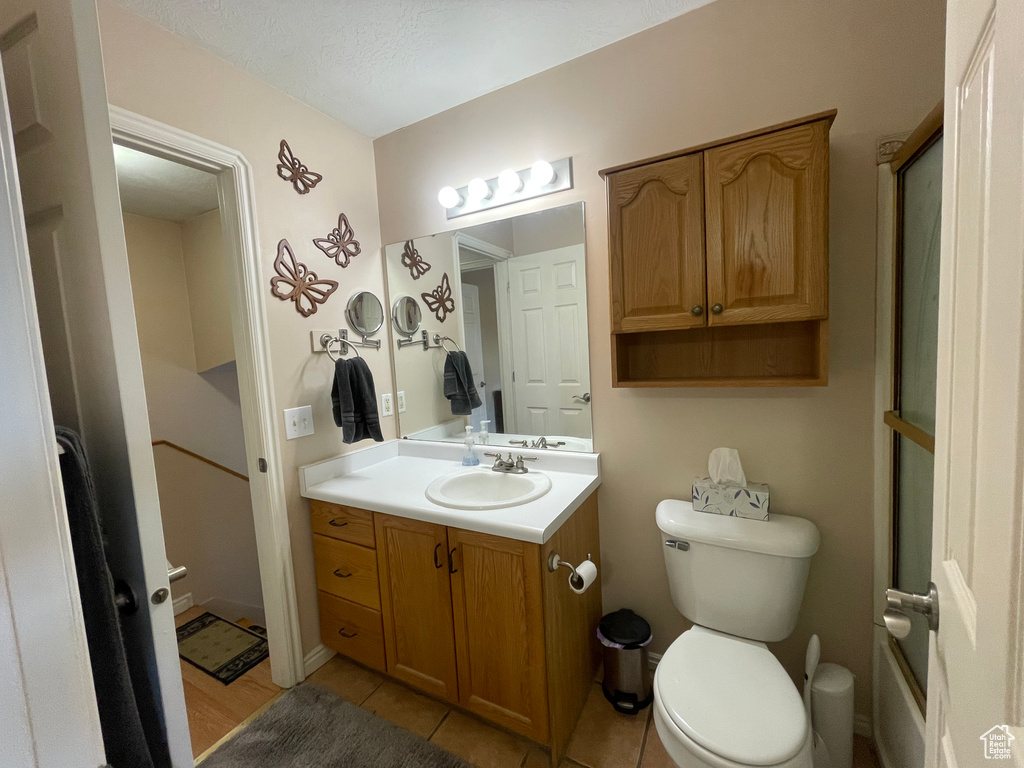 Bathroom with a shower with door, tile patterned floors, toilet, and vanity