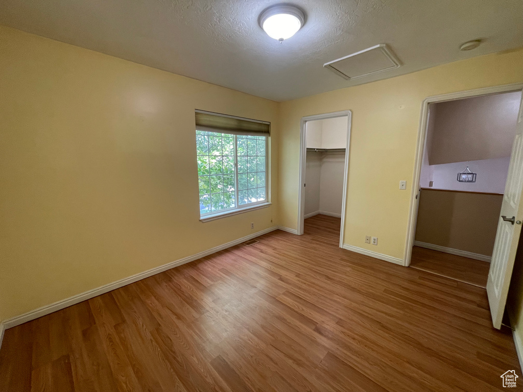 Unfurnished bedroom with hardwood / wood-style flooring, a closet, a textured ceiling, and a walk in closet