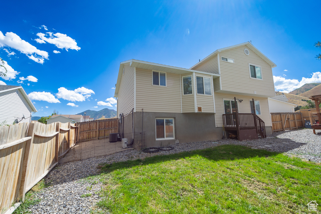 Back of house featuring central AC unit, a mountain view, and a lawn