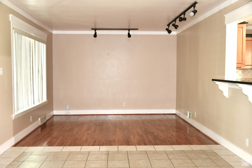 Empty room featuring light tile patterned flooring, ornamental molding, and track lighting