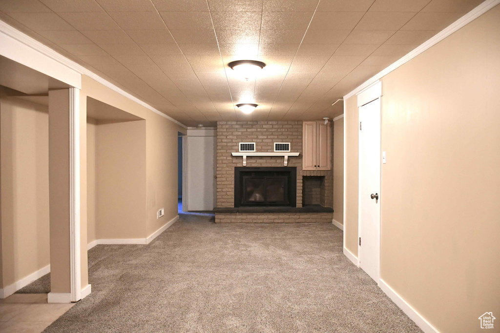 Basement with ornamental molding, a brick fireplace, and light carpet