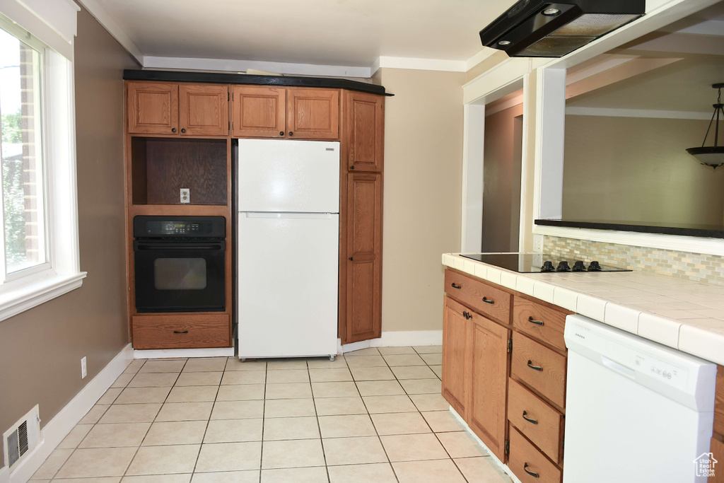 Kitchen with decorative backsplash, crown molding, black appliances, tile counters, and light tile patterned flooring