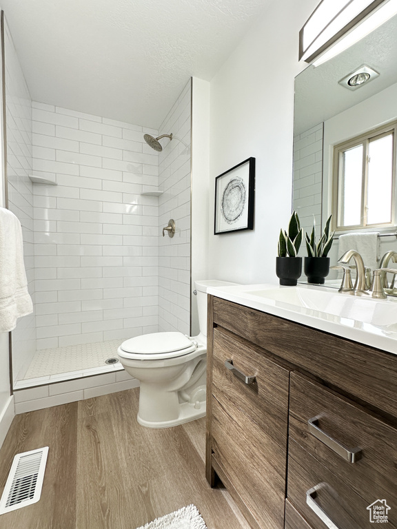 Bathroom featuring hardwood / wood-style flooring, a tile shower, a textured ceiling, vanity, and toilet