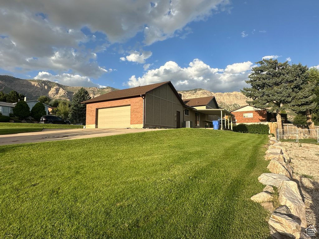 View of side of home featuring a lawn, a mountain view, and a garage