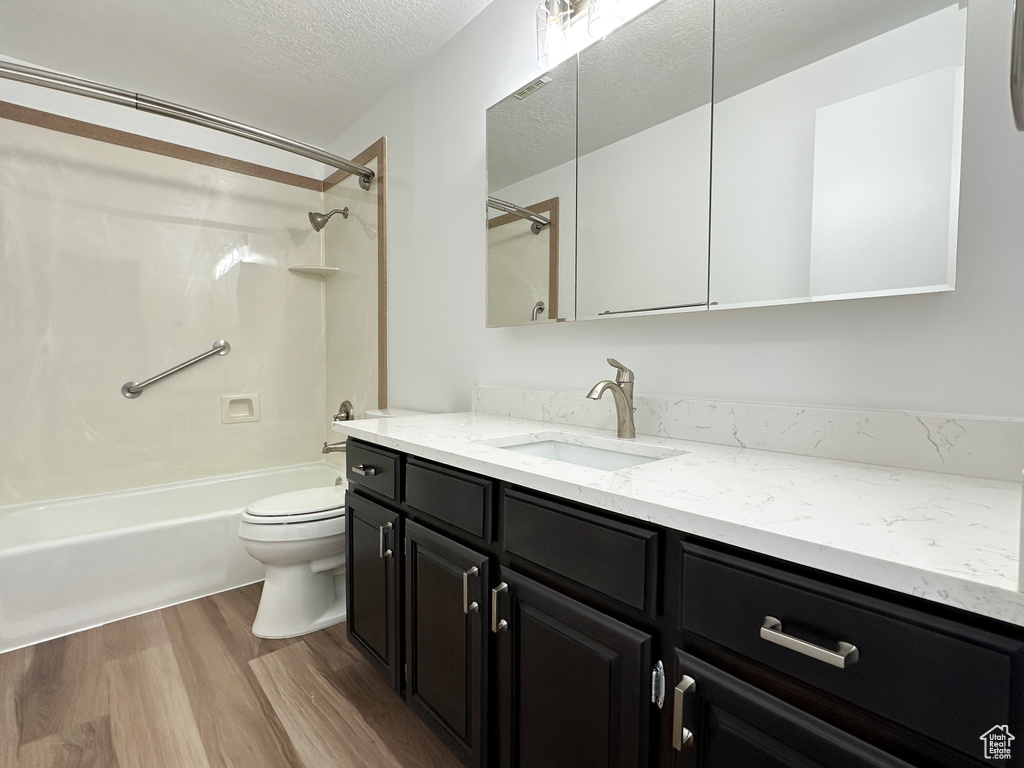 Full bathroom featuring hardwood / wood-style floors, vanity, a textured ceiling, shower / washtub combination, and toilet