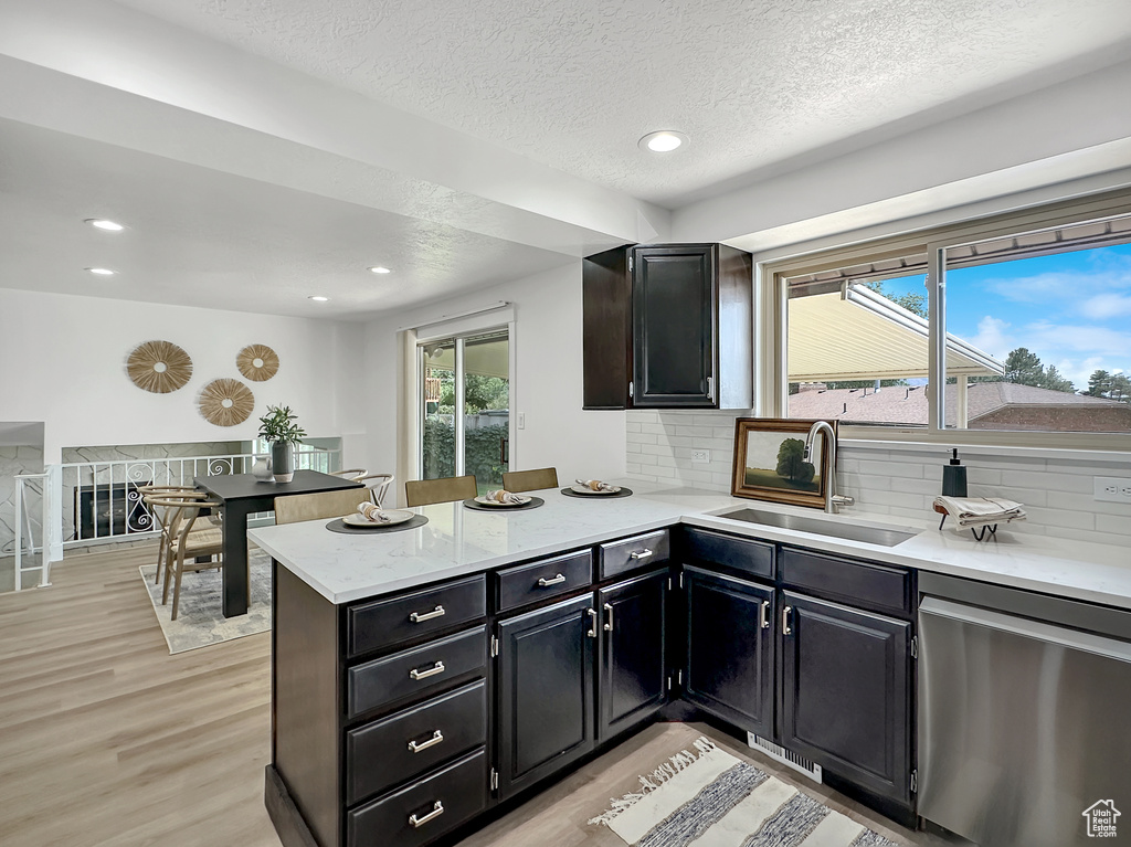 Kitchen featuring backsplash, sink, light hardwood / wood-style flooring, dishwasher, and kitchen peninsula