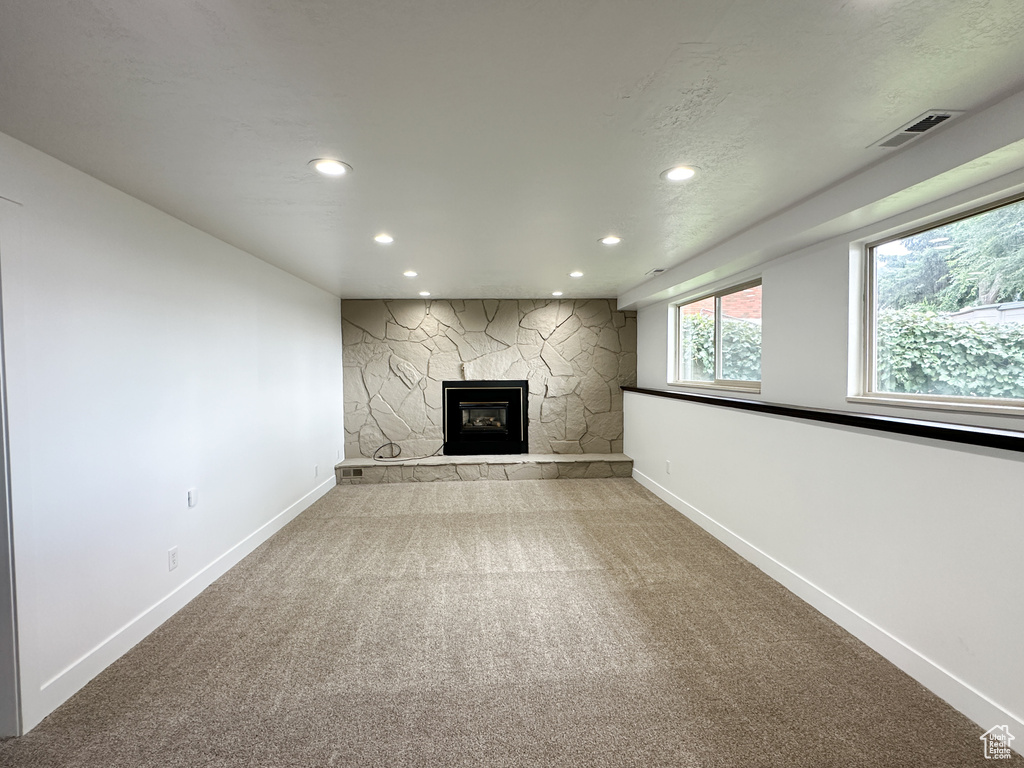 Unfurnished living room featuring light carpet and a stone fireplace