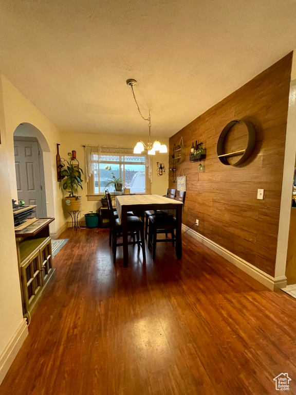 Dining area featuring dark hardwood / wood-style flooring, wooden walls, and an inviting chandelier