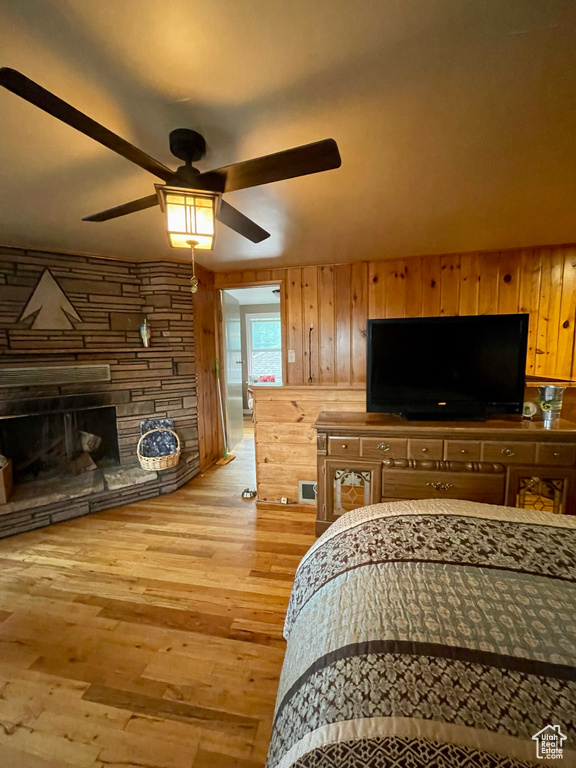 Bedroom featuring ceiling fan, wood walls, light hardwood / wood-style floors, and a stone fireplace