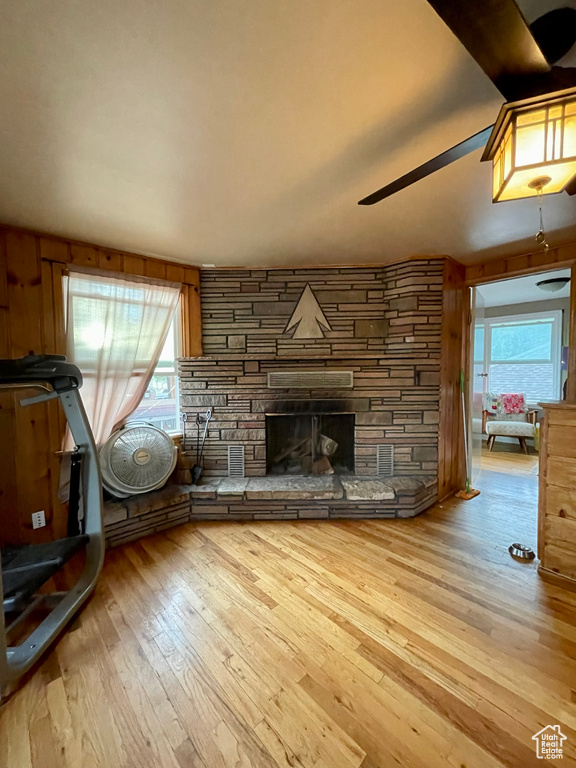 Unfurnished living room with ceiling fan, light hardwood / wood-style flooring, wooden walls, and a fireplace