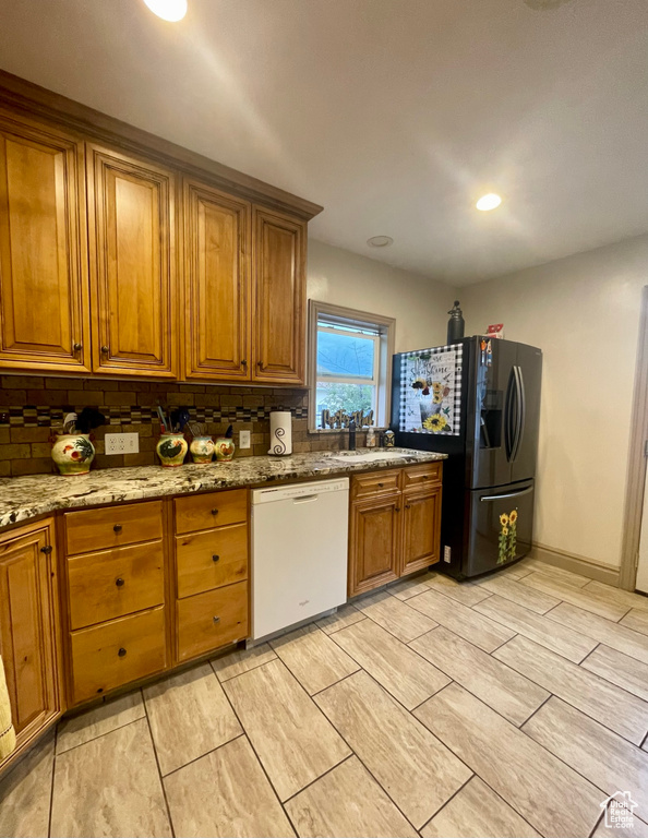 Kitchen featuring stainless steel refrigerator with ice dispenser, decorative backsplash, white dishwasher, and light stone countertops