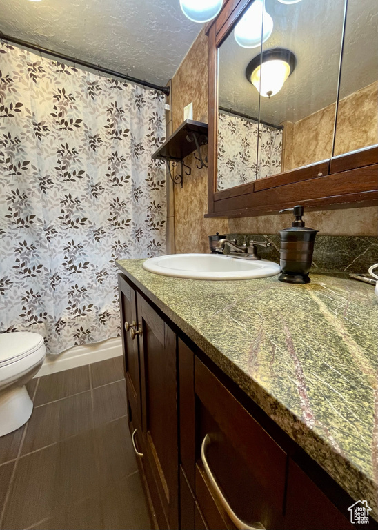 Bathroom with tile patterned floors, a textured ceiling, vanity, and toilet
