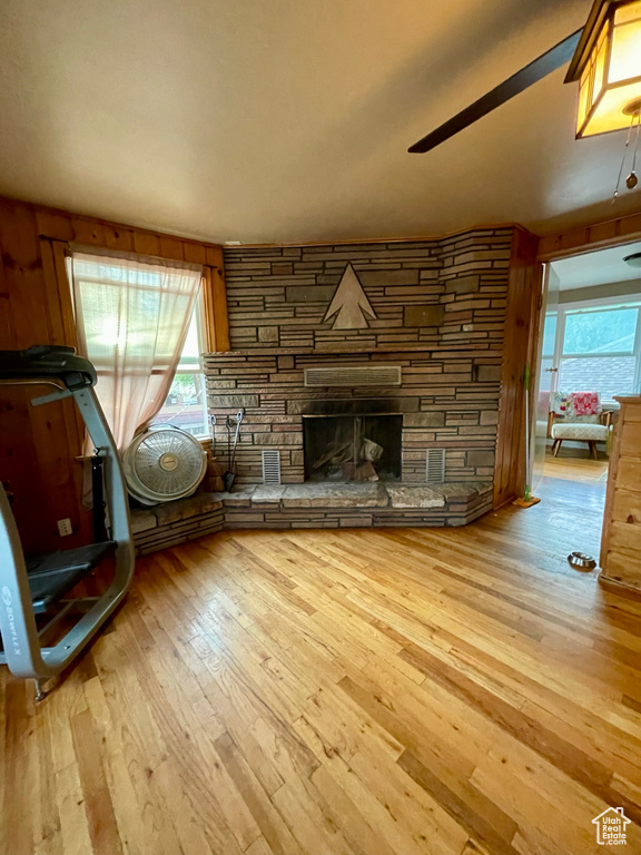 Unfurnished living room featuring light wood-type flooring, a wealth of natural light, wooden walls, and a fireplace