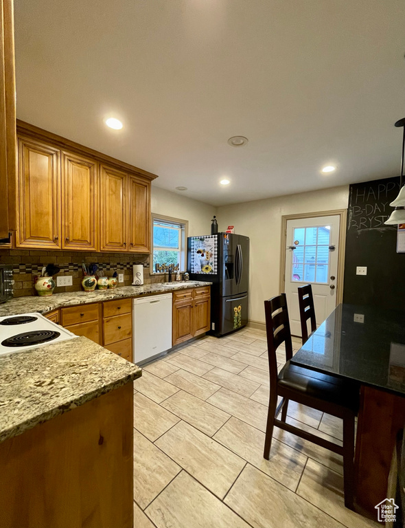 Kitchen featuring backsplash, white dishwasher, light stone counters, stainless steel refrigerator with ice dispenser, and light tile patterned floors
