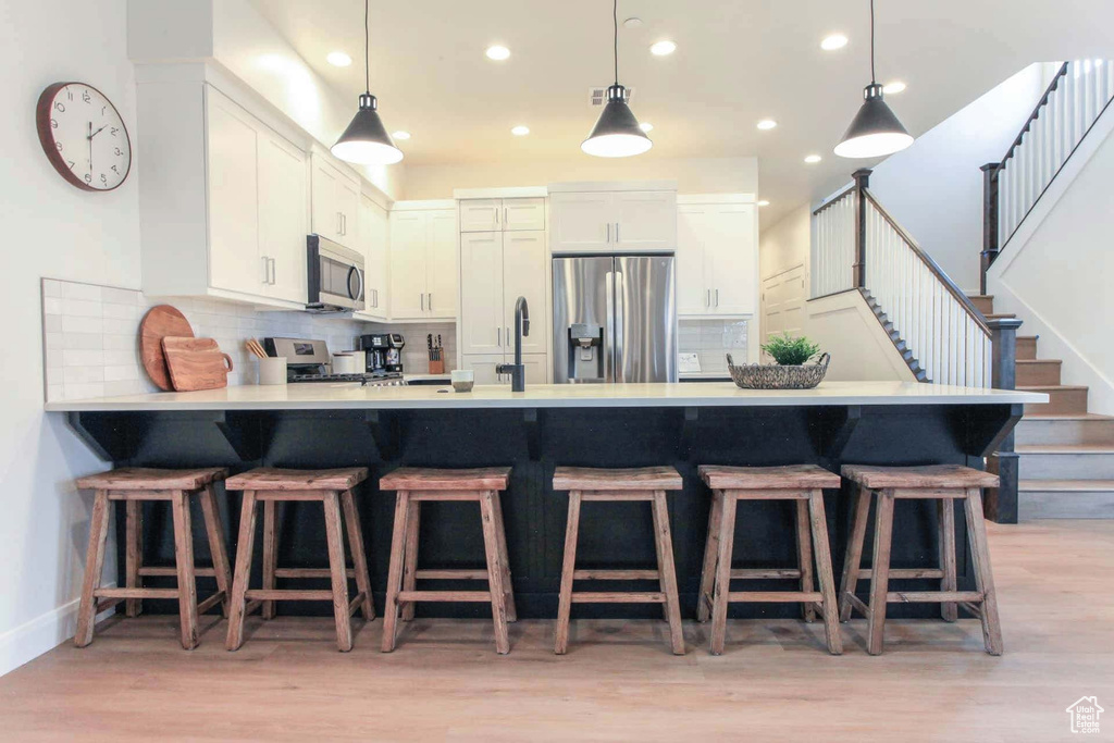 Kitchen with appliances with stainless steel finishes, light hardwood / wood-style flooring, decorative backsplash, and kitchen peninsula